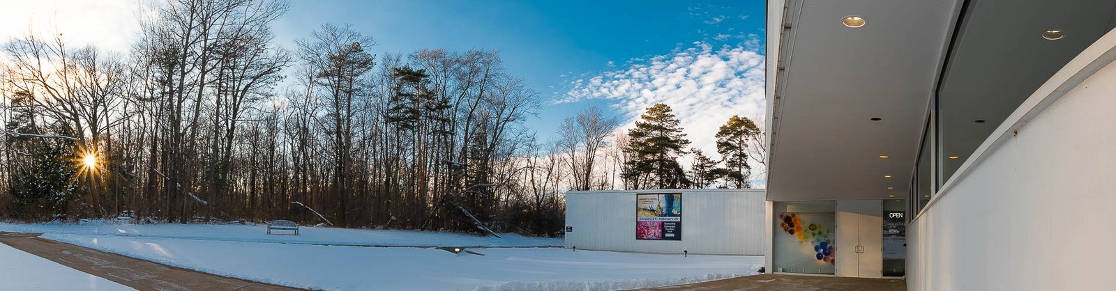 A cold snowy day showing the exterior of the Mansfield art center featuring the sidewalk leading up to door which has an open sign.